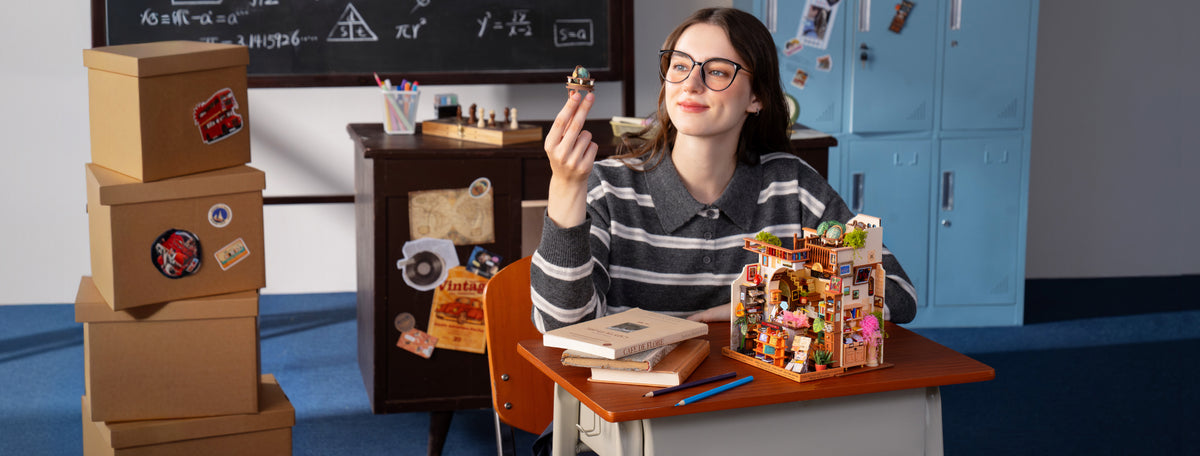Wide classroom scene with a woman waving beside the PageStory Books miniature and stacked boxes