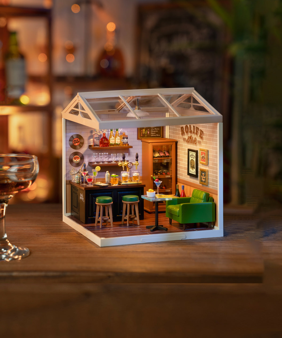 Rolife Super Creator miniature bar dollhouse with green sofa, beer taps, and warm lighting placed on a wooden table.