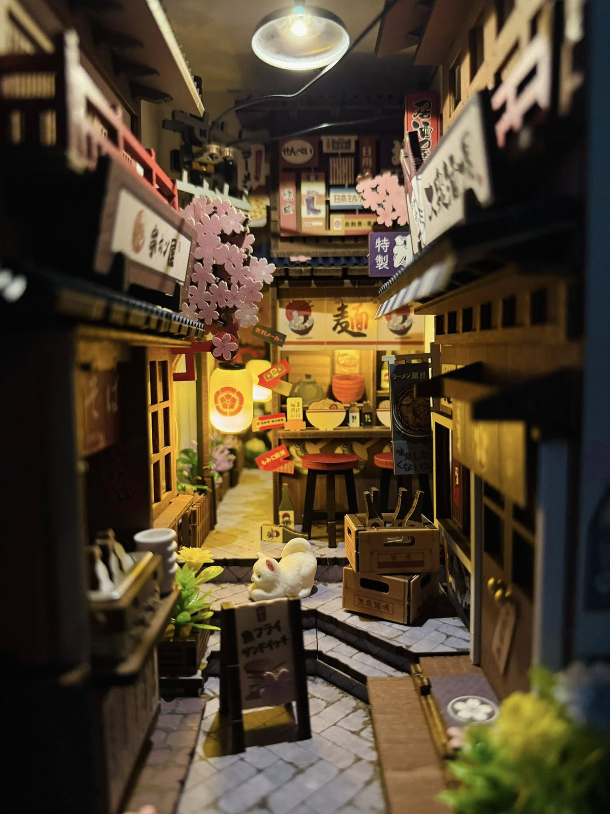 Rolife Sakura Wine Alley TGB11 book nook top-down interior view showing the alley depth with the white cat, crates, and yellow marigold flowers