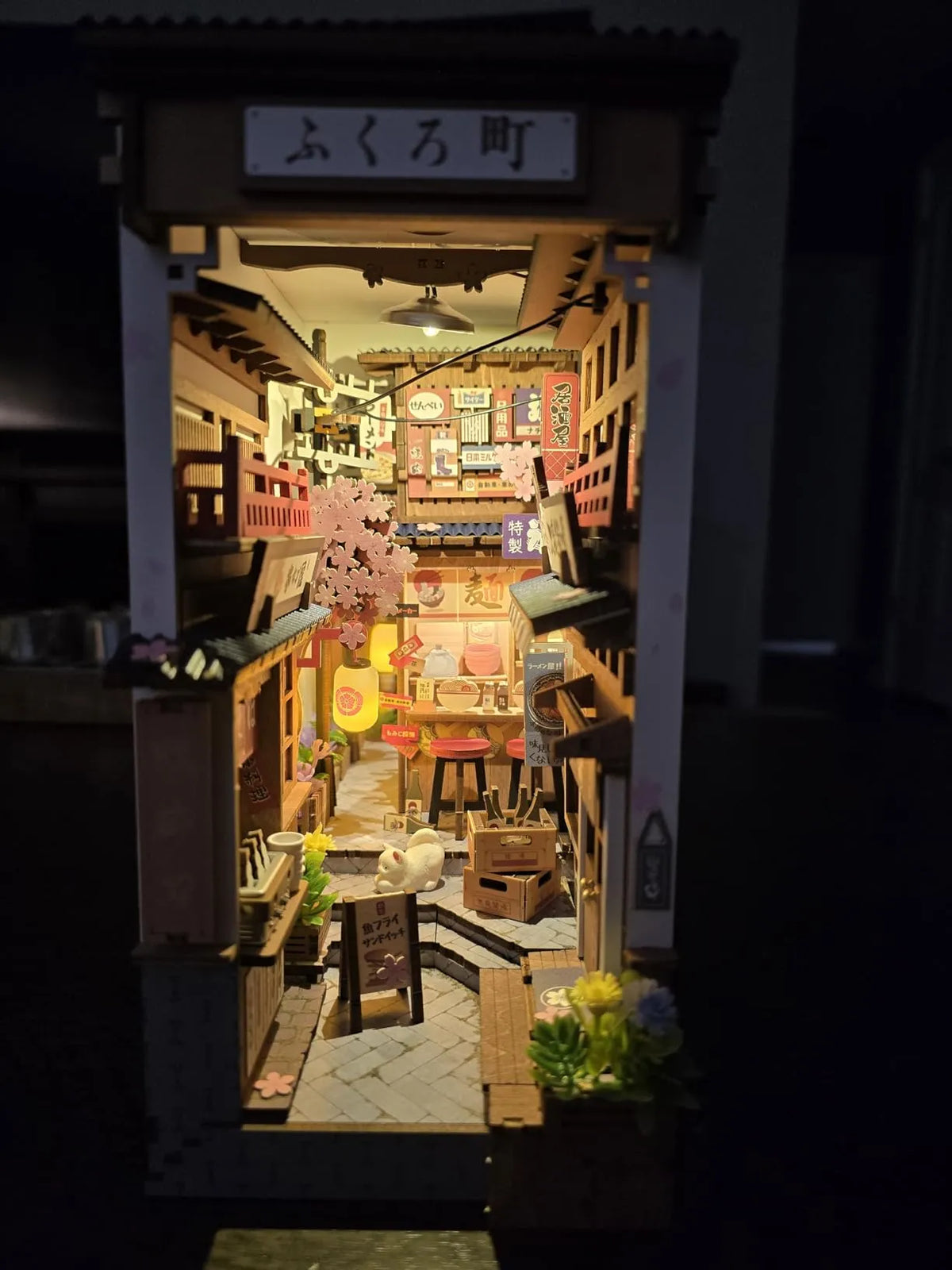 Rolife Sakura Wine Alley TGB11 book nook front view at night with glowing lantern, cherry blossom branches, and Japanese shop signs in a dark setting